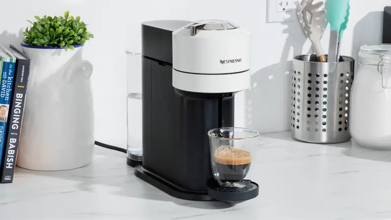 Nespresso Vertuo Next coffee maker on marble countertop next to potted plant and kitchen utensils.