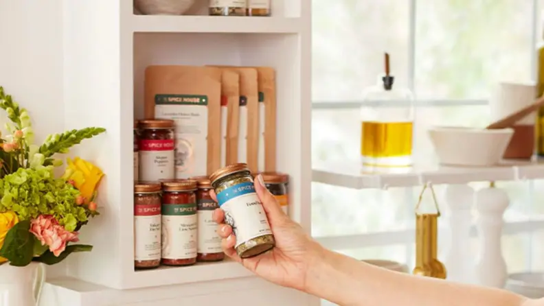 A hand pulling a Spice House jar out of a cabinet filled with similar products.