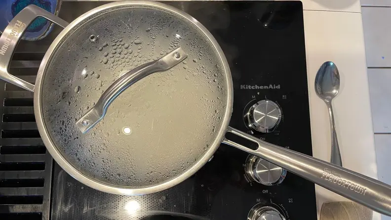 A Guy Fieri Flavortown Laser Titanium pot with lid attached boiling on top of cooktop.