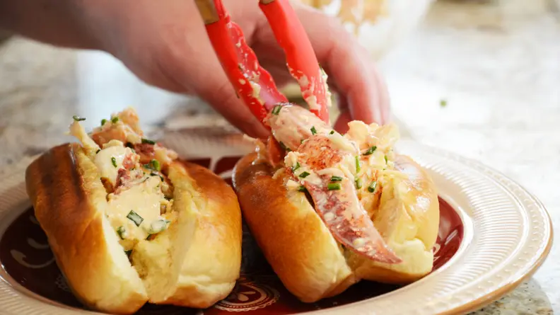 A person is using a pair of tongs to stuff the sandwich buns with lobster salad.
