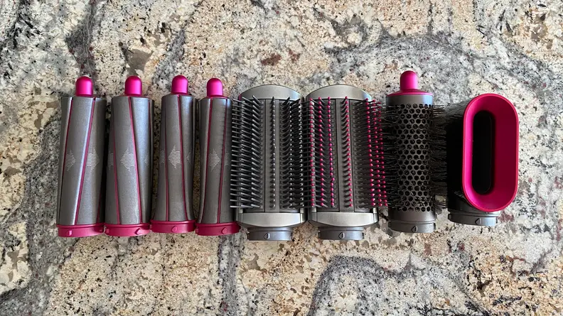 The Dyson Airwrap Styler attachments against a granite countertop. From left to right: the curling wands, the smoothing brushes, and the pre-styler dryer.