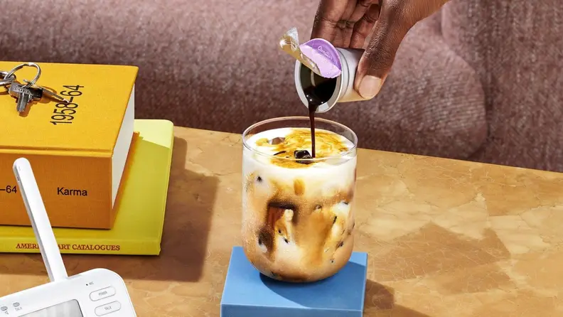 Hand pouring Cometeer concentrate into an iced latte, on a coffee table