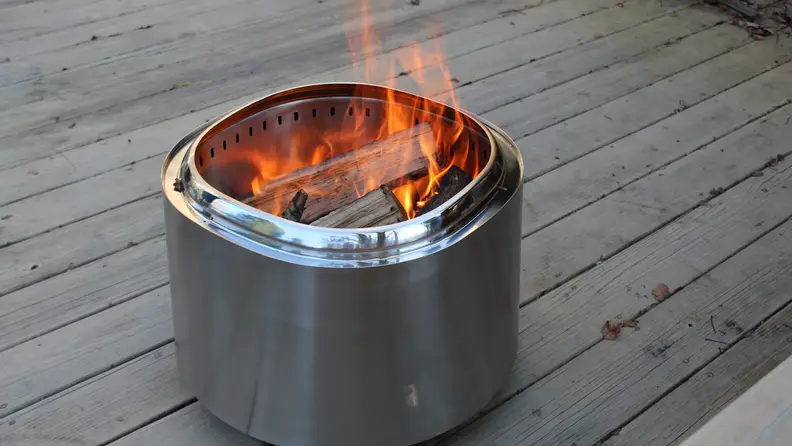 The East Oak fire pit on a wood deck with a fire burning inside and visible logs.