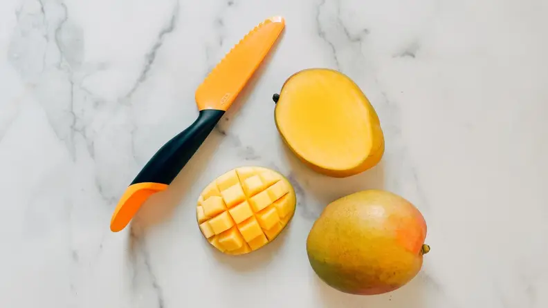 An OXO mango slicer sits on a marble surface next to two mango halves.