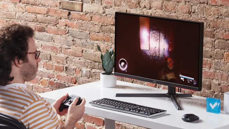 A man holding a controller, playing a game on the AOC Q27GX3MN.