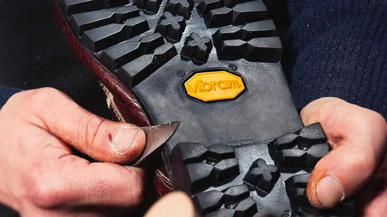 A man carving the bottom of a Vibram outsole to repair it.