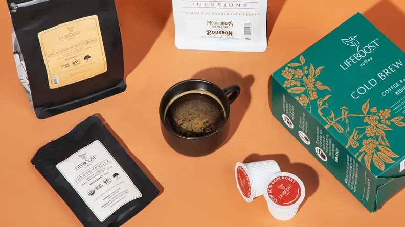 A cup of coffee next to Lifeboost Coffee products on an orange background.
