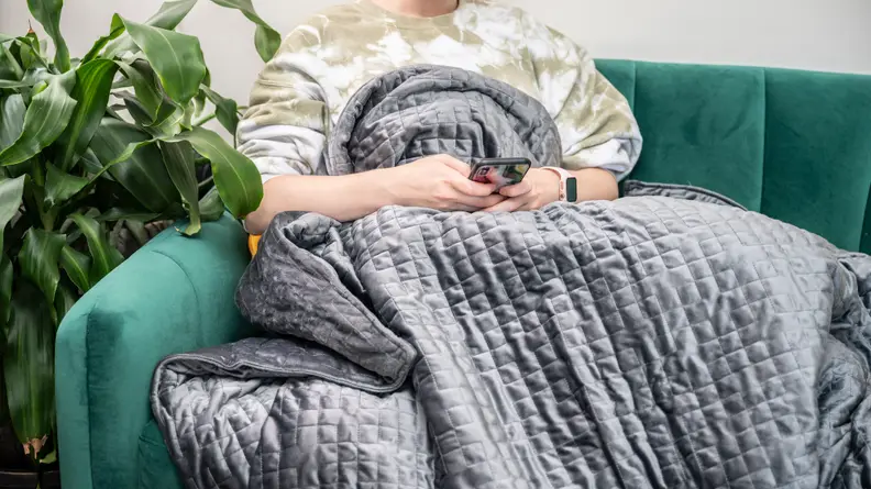 a woman sits under the gravity blanket on a green couch