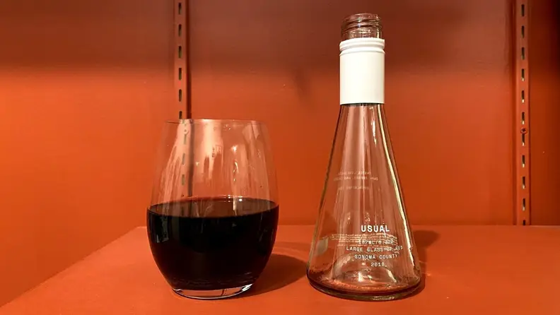 A Usual Wines bottle emptied into a wine glass, which is over halfway full.