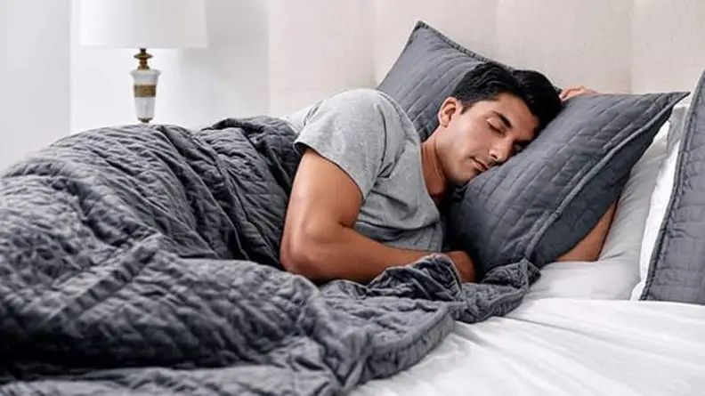 A man sleeping in a bed, covered in a weighted blanket.