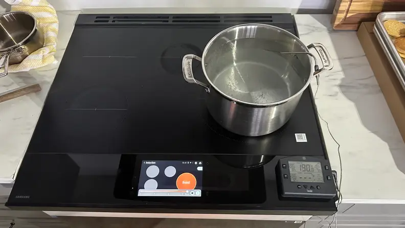 A pot of boiling water sits on the cooktop of the Samsung Bespoke NSI6DB990012AA Induction Range with a digital screen showing a red circle for the burner that's on.