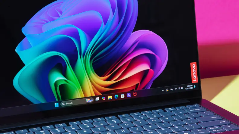 A closer angled view of the screen and keyboard on the Lenovo Yoga Slim 7x laptop with a colorful screensaver on screen.
