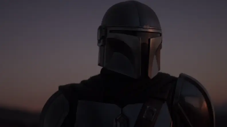 A screenshot from The Mandalorian series featuring the Mandalorian himself against a dark background.