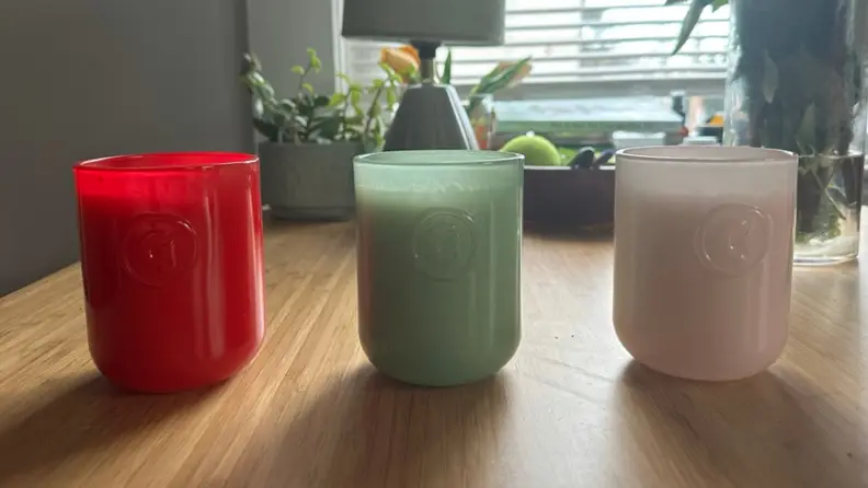 The three different Glossier candles lined up in a row on a table.