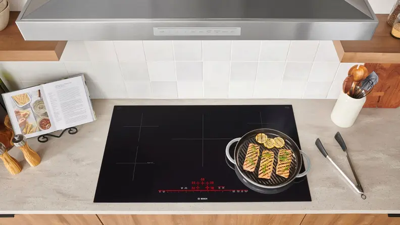 A top-down photo of an induction cooktop with a pan filled with fish cooking on top.