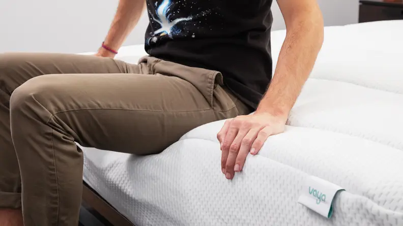A person sitting on the edge of the mattress as it sinks down.