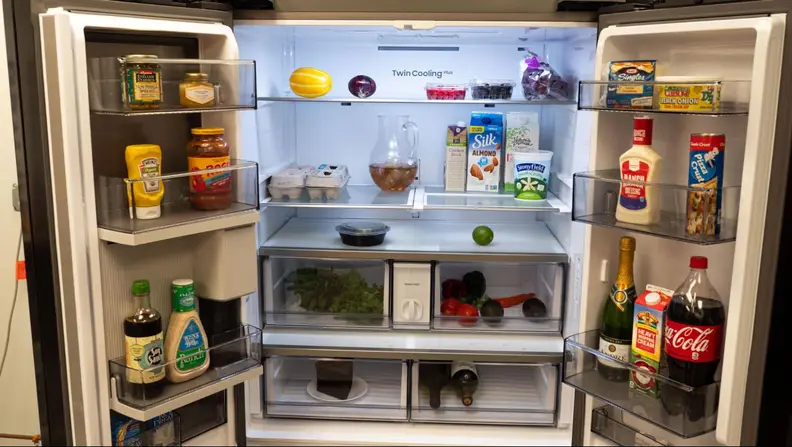 The french doors of a Samsung RF30 open showing inside fully stocked storage shelves and compartments.
