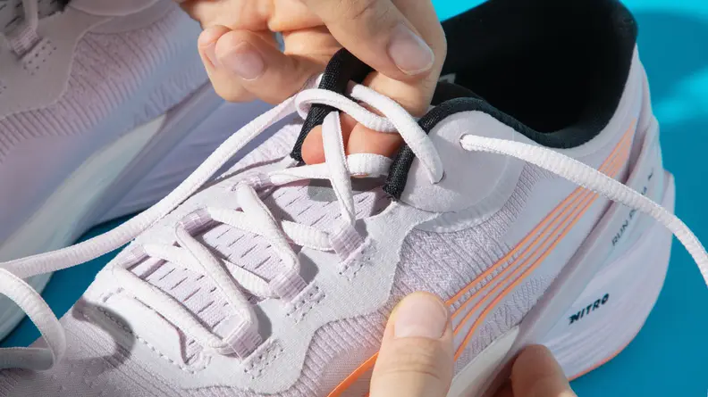 A person loosens the laces on a pair of Puma Run XX Nitro running shoes.