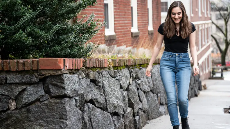 A woman walking down the street in a black short sleeve shirt and Good American skinny jeans