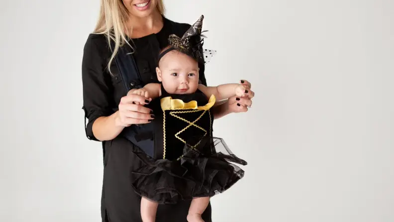 A parent holds an infant in a witch Halloween costume.