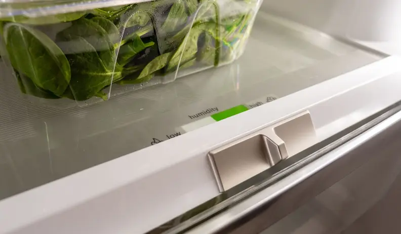 The humidity slide on a Bosch fridge crisper drawer below a plastic container of greens.