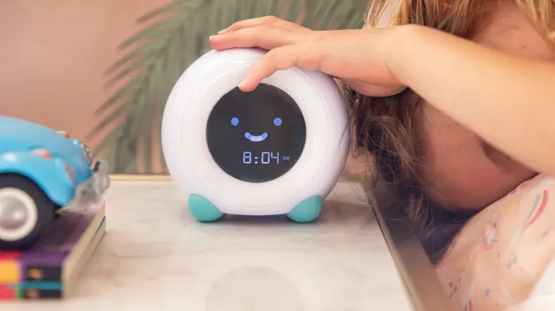 A LittleHippo Mella alarm clock sitting on a bedside table with a child's hand on top.
