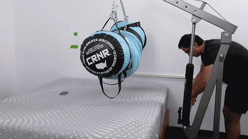 A person lowering a weighted punching bag onto the Sealy Posturepedic mattress to test its absorbency.