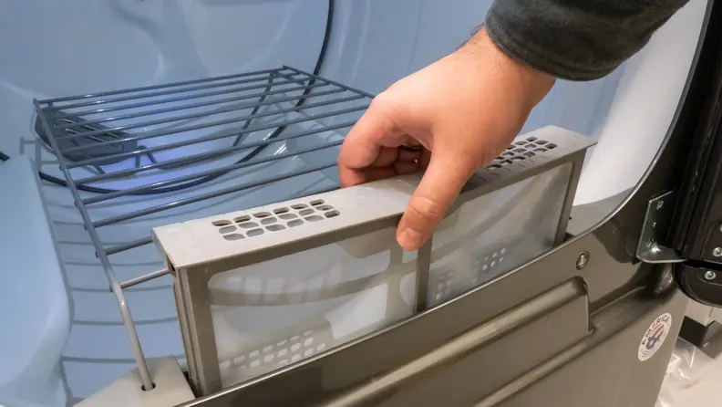 A hand reaches into frame to either remove or reinsert the lint trap. It is unclear from the image and the mystery shall live on throughout time.