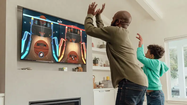 a child and adult miming a basketball throw motion while a basketball game is shown on TV