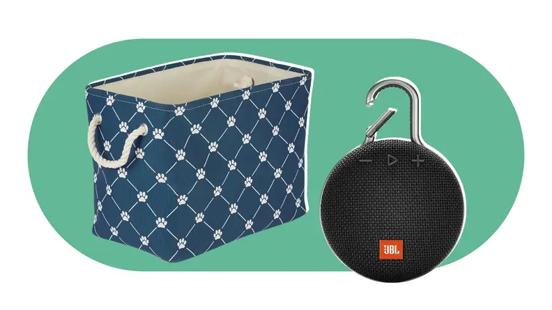 A navy storage box with paw prints printed on exterior and rope handles next to black portable speaker with clip on top..