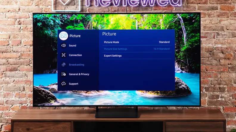 The Samsung S90C QD-OLED TV on an entertainment center with a brick background.
