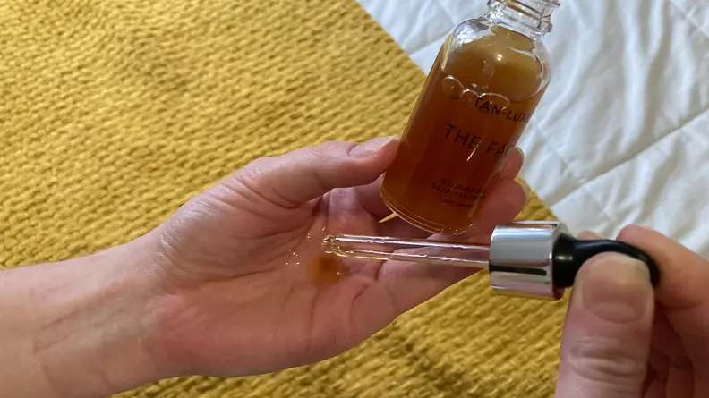 Person squeezing serum into palm of hand while holding bottle.