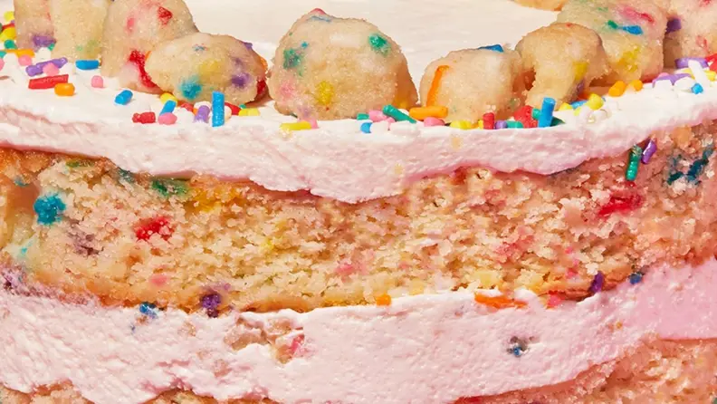 A closeup image of funfetti birthday cake with layers of creamy vanilla frosting.
