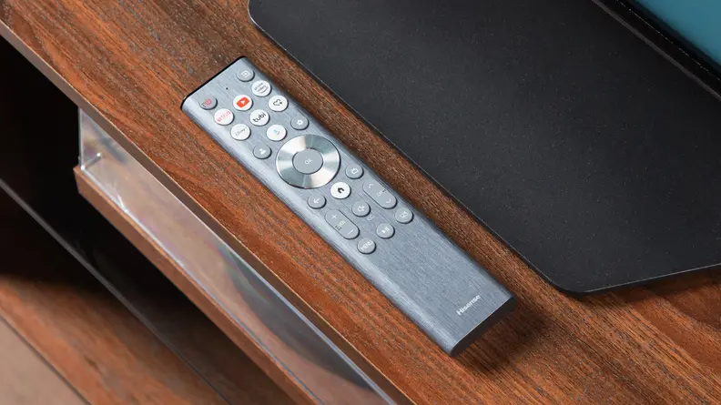 The Hisense U8N's chrome-accented remote control placed on a wooden media console in front of the TV's stand
