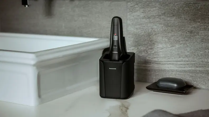 The Panasonic Arc6 electric razor in its charging dock on top of a sink vanity.