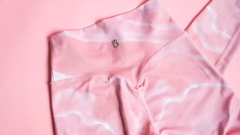 A close-up of the back of a pair of pink leggings on a pink background.