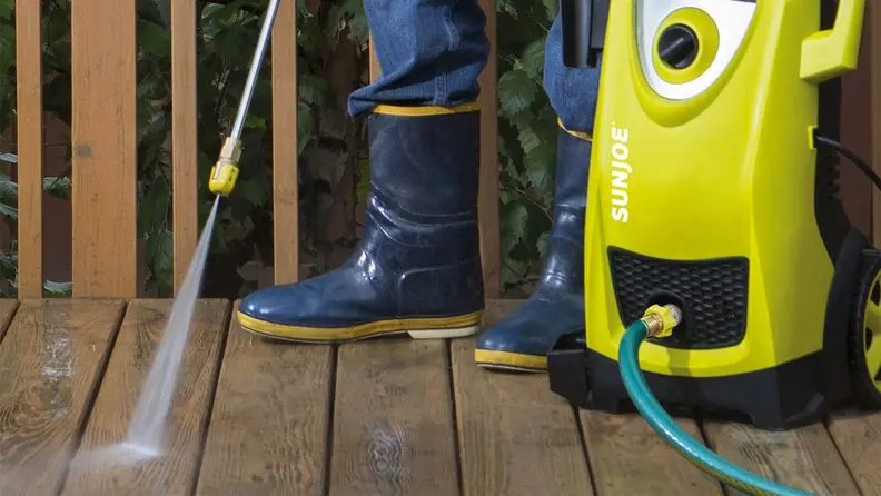 A person power washes a deck.