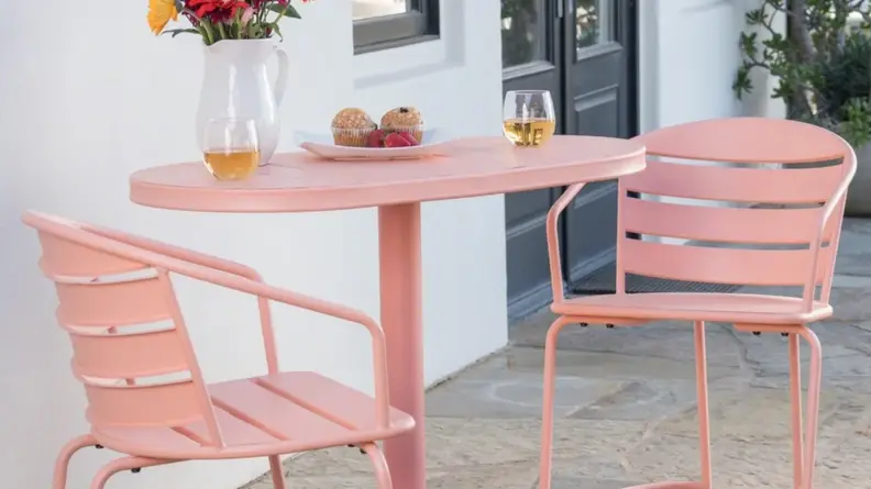 A pink bistro table and chairs sit on a patio.