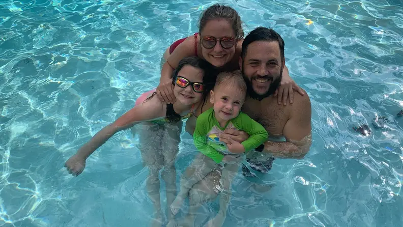 A family of four smiles together in a swimming pool.