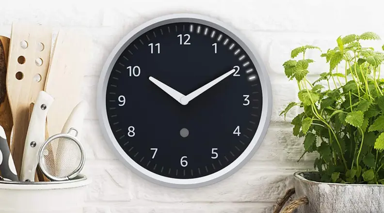The Echo Wall Clock hangs in a kitchen next to herbs and cooking utensils.