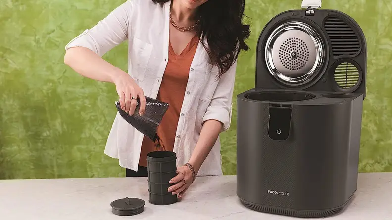 A person pour compost into a Vitamix Eco 5 FoodCycler cup, next to the Vitamix Eco 5 FoodCycler machine.