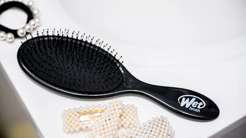 One of the best hair brushes from Wet Brush sitting on a sink with hair clips next to it.