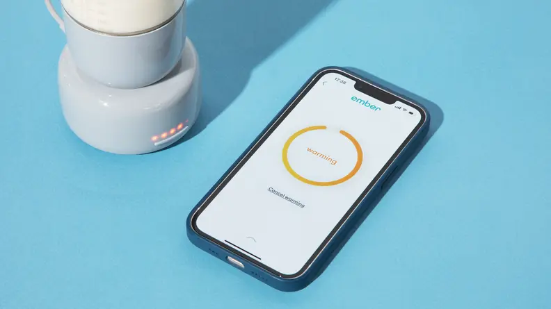 The Ember Baby Bottle System next to a smart phone on a blue background.