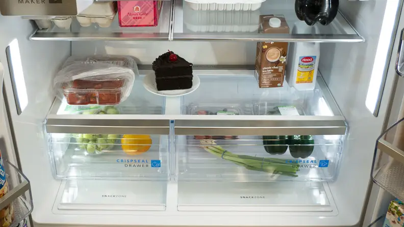 The lower, interior portion of a fridge with crisper drawers filled with grapefruit and green onions