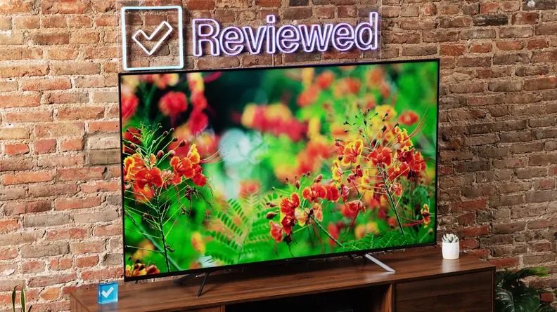 The Hisense U7H displaying flowers as it sits on a wooden table in front of a brick wall.