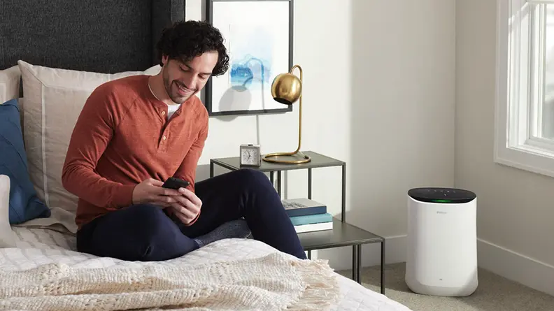 Person sitting on top of bed in bedroom while smiling at smartphone.
