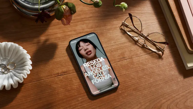 A smartphone on a wooden desk displays a sleek website built with Squarespace templates next to glasses and a ring dish.