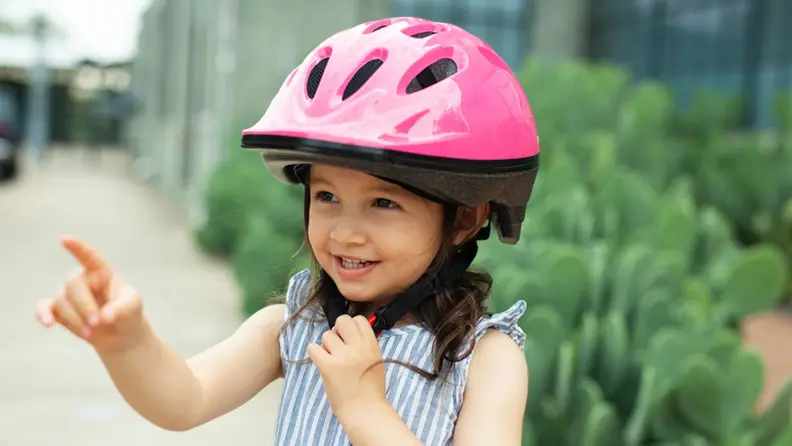 A little girl smiles with her pink Joovy helmet