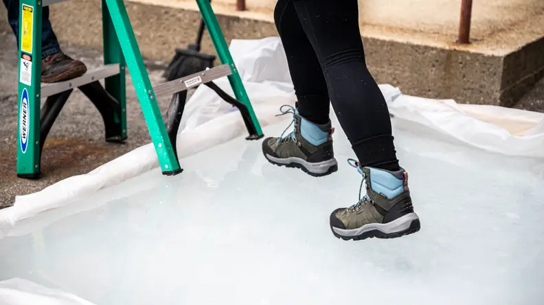 A woman is testing the traction of a pair of winter boots on a small outdoor ice rink.