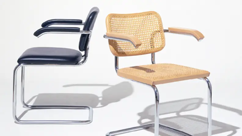 Two Cesca chairs with arms. One with blue upholstery and one made of cane.